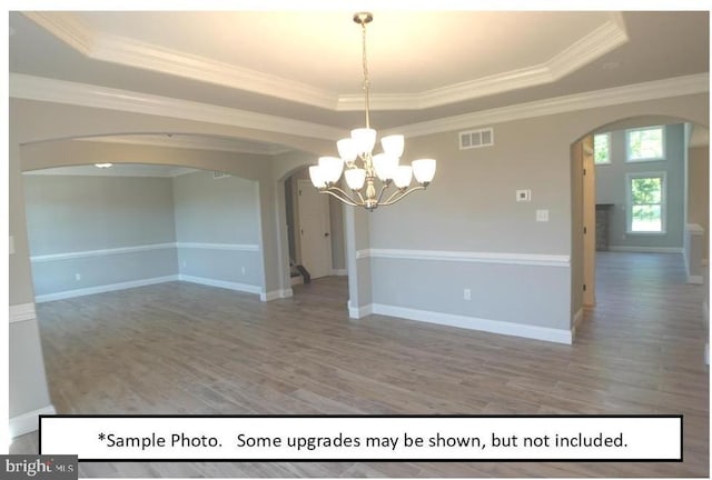 unfurnished room with ornamental molding, a raised ceiling, hardwood / wood-style floors, and a notable chandelier