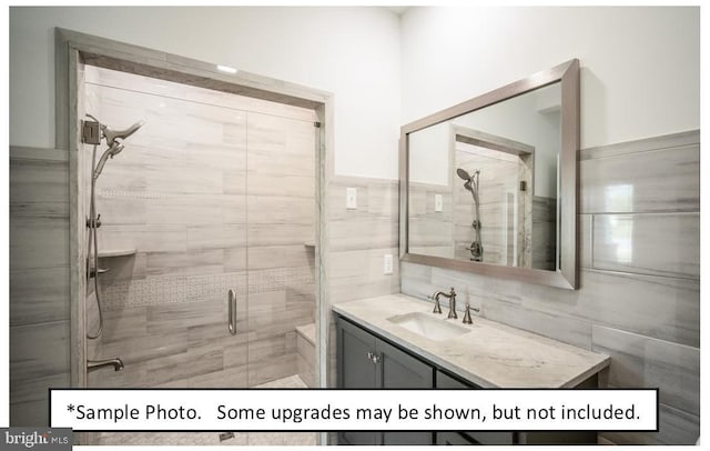 bathroom with vanity, a shower with door, and tile walls