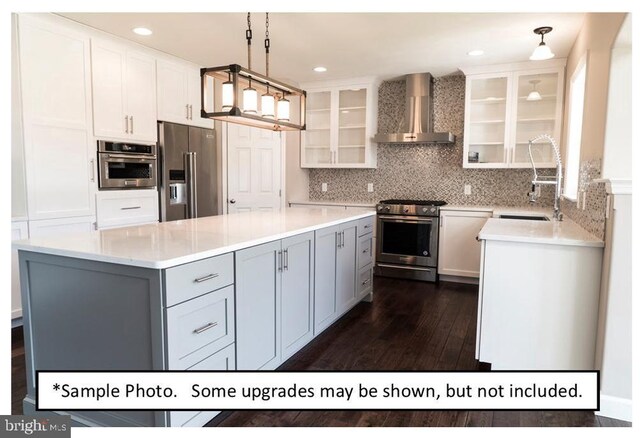 kitchen featuring wall chimney range hood, a kitchen island, stainless steel appliances, decorative backsplash, and pendant lighting