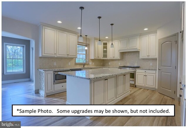 kitchen with appliances with stainless steel finishes, tasteful backsplash, decorative light fixtures, a kitchen island, and custom range hood