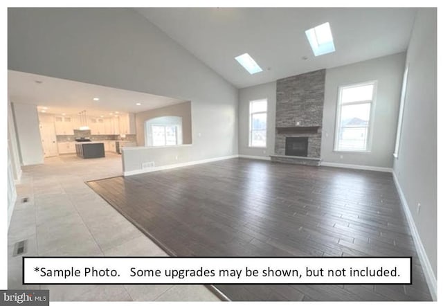 unfurnished living room with hardwood / wood-style flooring, high vaulted ceiling, a fireplace, and a skylight