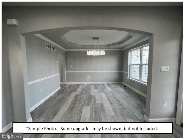 unfurnished dining area featuring a raised ceiling, ornamental molding, hardwood / wood-style flooring, and an inviting chandelier