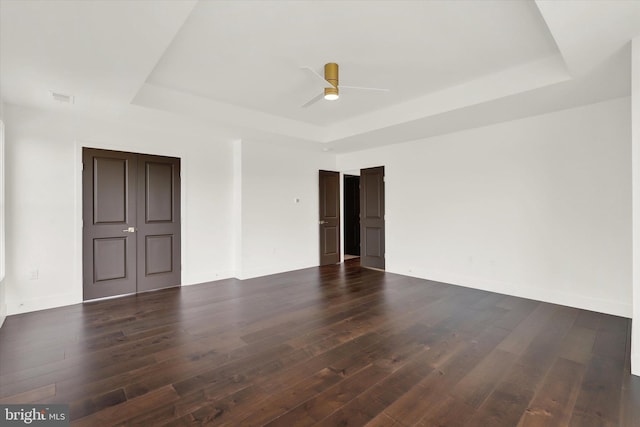 spare room featuring dark wood-type flooring, a raised ceiling, and ceiling fan