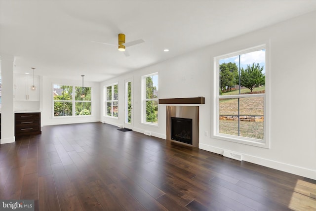 unfurnished living room featuring ceiling fan, a wealth of natural light, and dark hardwood / wood-style flooring