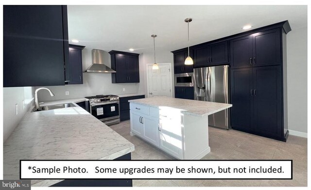 kitchen with wall chimney range hood, stainless steel appliances, hanging light fixtures, sink, and a kitchen island