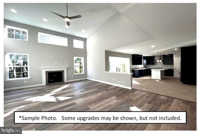 unfurnished living room with wood-type flooring, a towering ceiling, and ceiling fan