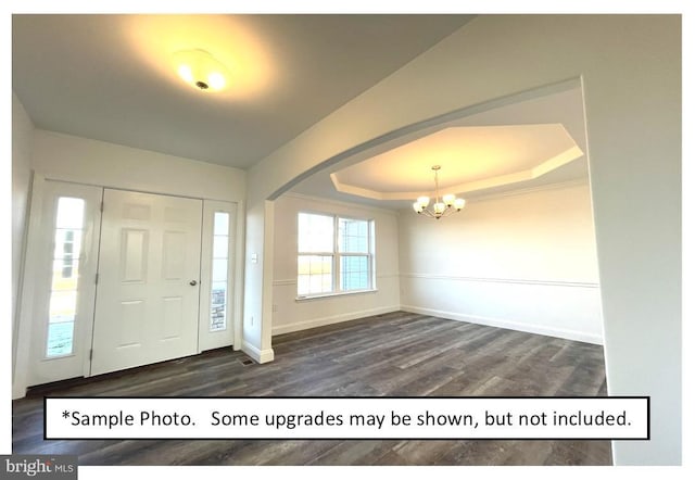 foyer entrance featuring an inviting chandelier, dark hardwood / wood-style floors, and a tray ceiling