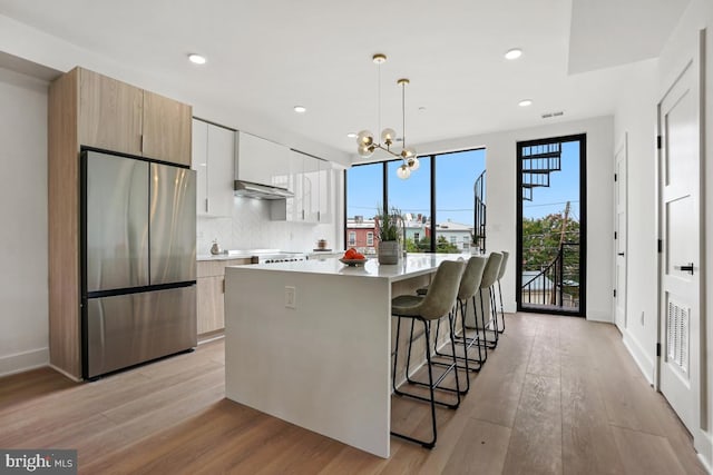 kitchen with pendant lighting, white cabinetry, stainless steel fridge, a kitchen bar, and a center island