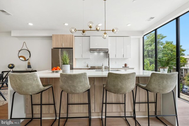 kitchen featuring white cabinetry, decorative backsplash, light hardwood / wood-style floors, a kitchen breakfast bar, and a kitchen island with sink