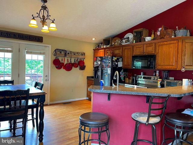 kitchen featuring pendant lighting, sink, a kitchen bar, black appliances, and light hardwood / wood-style flooring