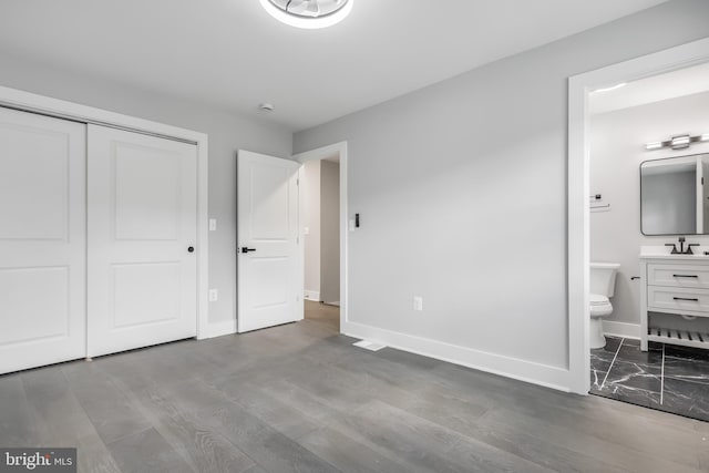 unfurnished bedroom featuring sink, a closet, connected bathroom, and wood-type flooring