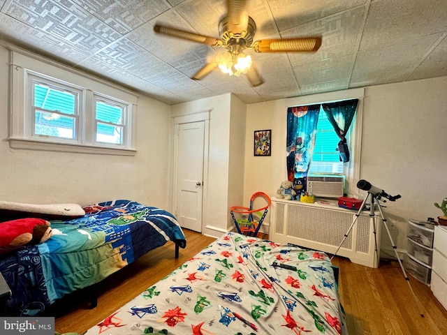 bedroom with light hardwood / wood-style floors, ceiling fan, radiator heating unit, and cooling unit