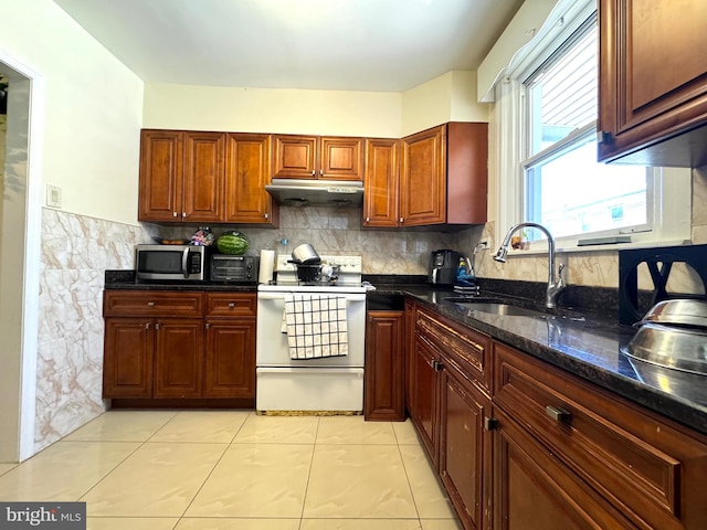 kitchen with dark stone counters, decorative backsplash, white range with electric stovetop, sink, and light tile patterned flooring