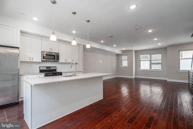 kitchen featuring sink, white cabinetry, appliances with stainless steel finishes, pendant lighting, and a kitchen island with sink