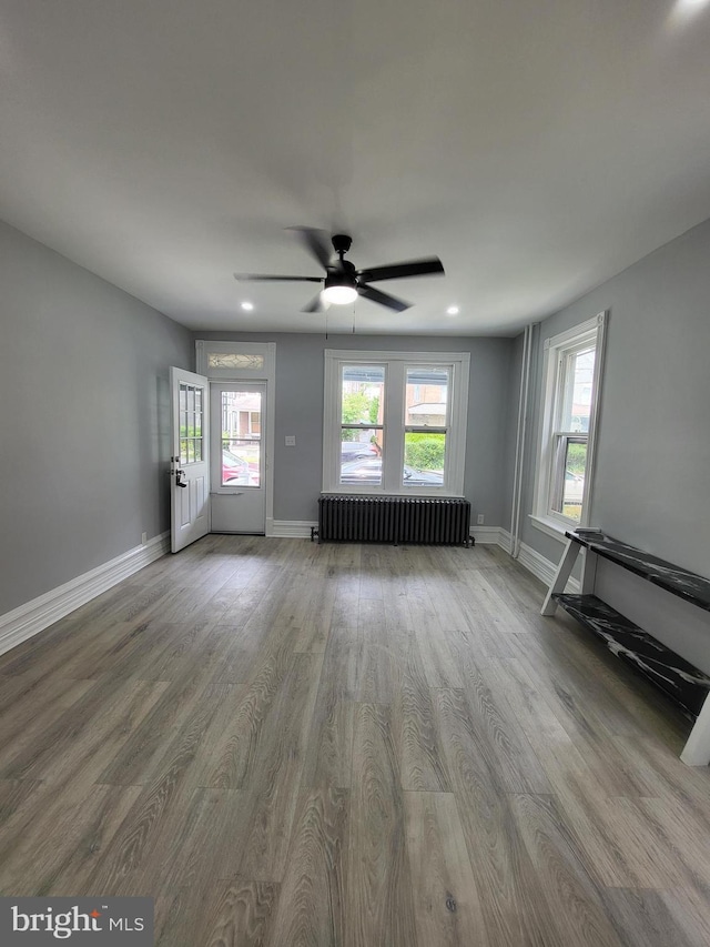 unfurnished living room with ceiling fan, a healthy amount of sunlight, radiator heating unit, and light hardwood / wood-style flooring