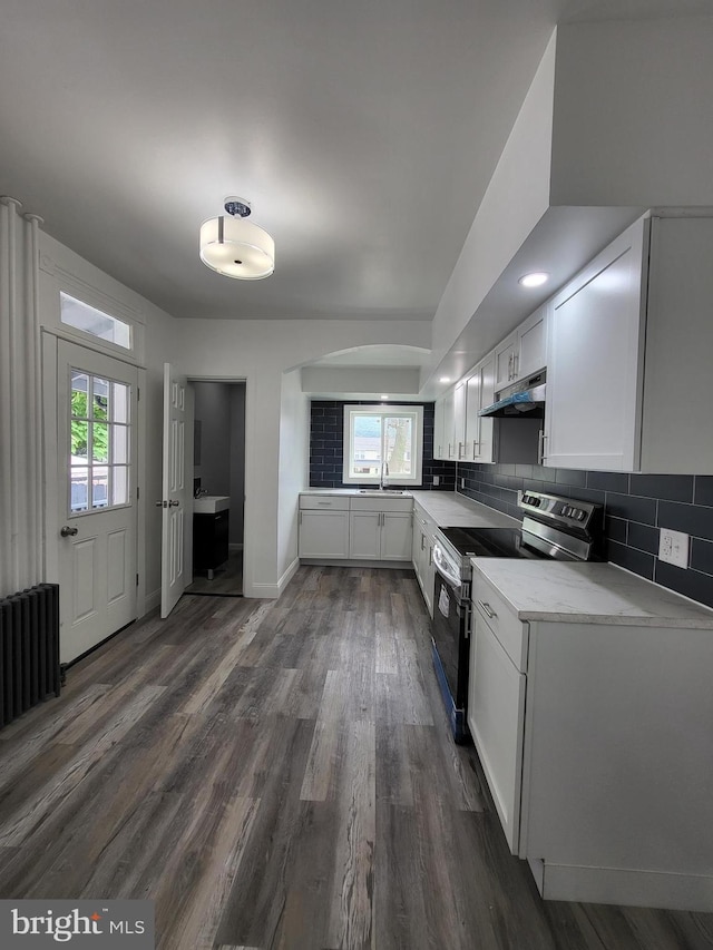 kitchen with stainless steel range with electric cooktop, white cabinetry, radiator heating unit, dark hardwood / wood-style floors, and backsplash