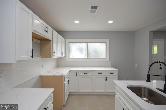 kitchen with sink, white cabinets, a wealth of natural light, and light stone countertops