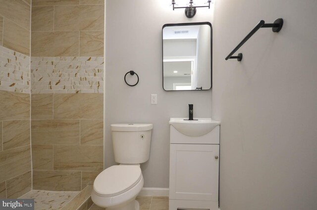 bathroom with vanity, tiled shower, tile patterned flooring, and toilet