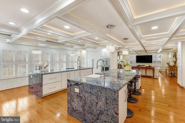 kitchen featuring a spacious island, decorative light fixtures, white cabinets, dark stone counters, and light hardwood / wood-style floors