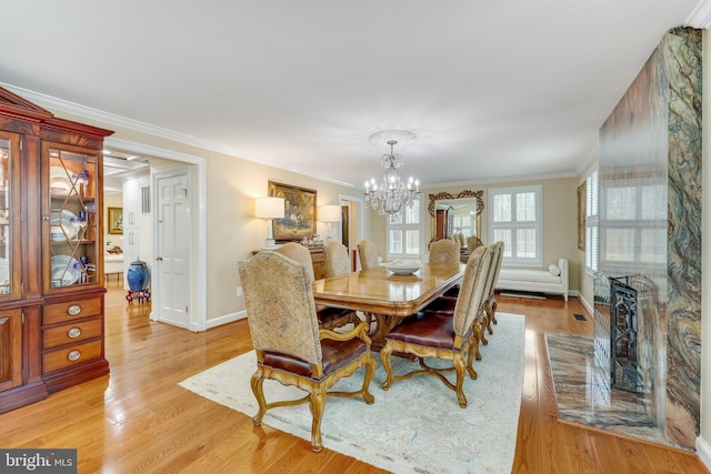 dining space featuring light hardwood / wood-style floors, a large fireplace, ornamental molding, and an inviting chandelier