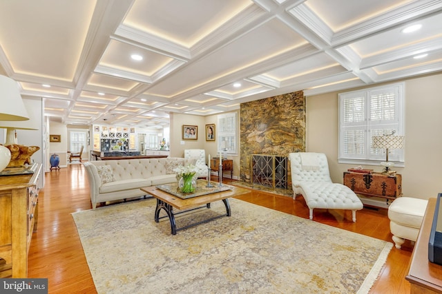 living room featuring coffered ceiling, light hardwood / wood-style floors, beamed ceiling, and a stone fireplace