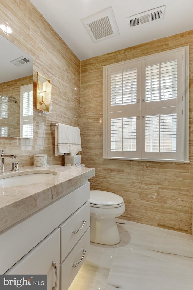 bathroom featuring tile patterned flooring, vanity, a shower, tile walls, and toilet