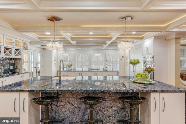 kitchen featuring decorative light fixtures, a large island with sink, dark stone counters, and an inviting chandelier