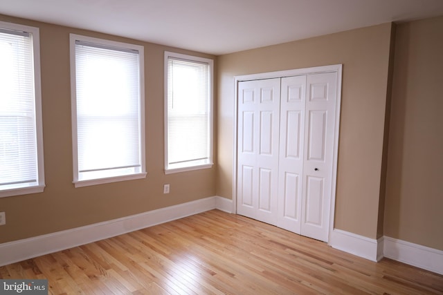 unfurnished bedroom with light wood-type flooring, a closet, and multiple windows