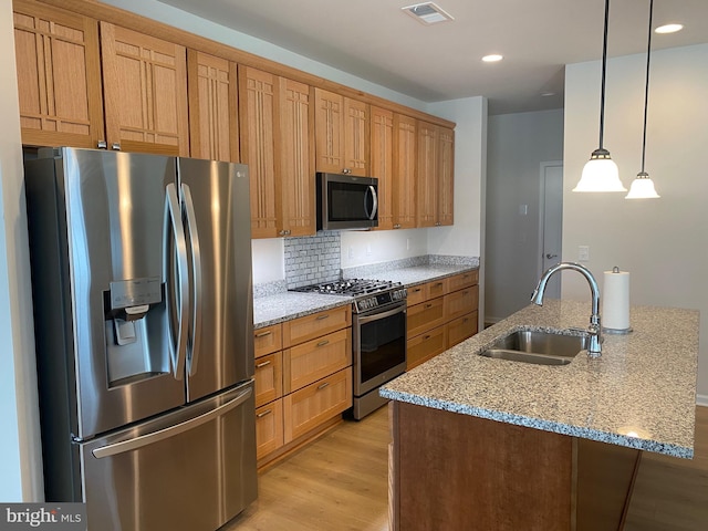 kitchen with light stone counters, appliances with stainless steel finishes, light hardwood / wood-style flooring, pendant lighting, and sink