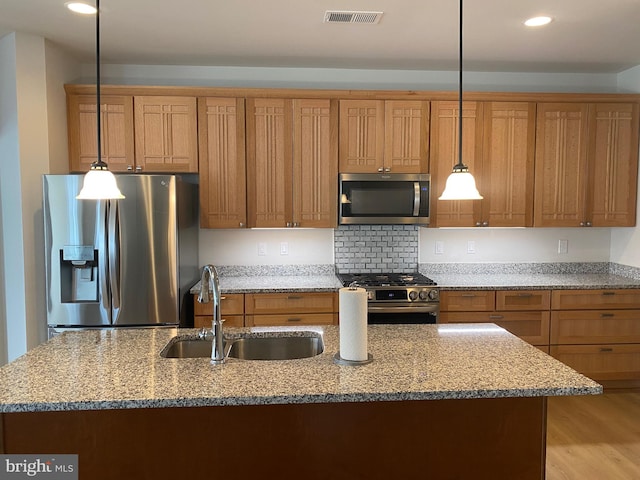 kitchen with appliances with stainless steel finishes, sink, decorative light fixtures, light stone counters, and light hardwood / wood-style flooring