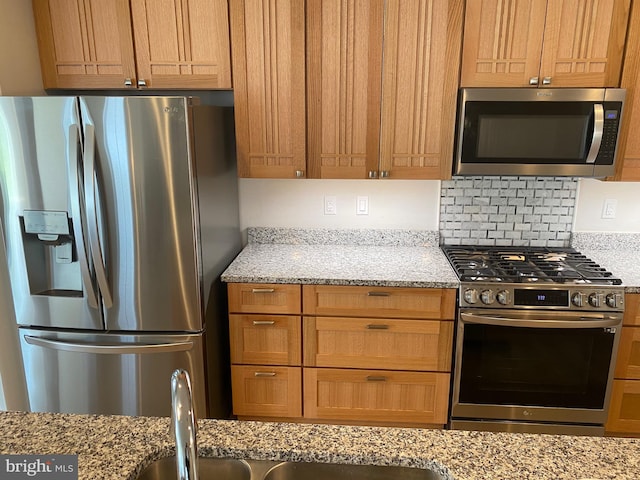 kitchen with light stone counters, appliances with stainless steel finishes, and backsplash