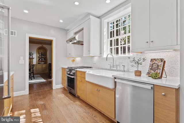 kitchen featuring appliances with stainless steel finishes, sink, wall chimney range hood, and white cabinets