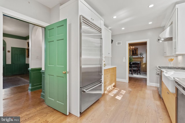 kitchen with white cabinetry, high end appliances, light wood-type flooring, and wall chimney exhaust hood