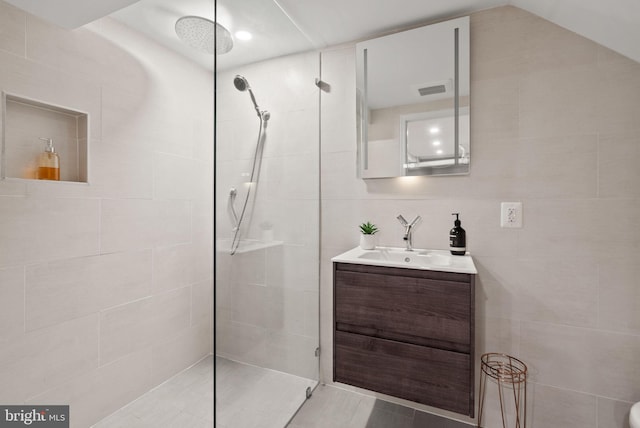 bathroom with a tile shower, vanity, and tile walls