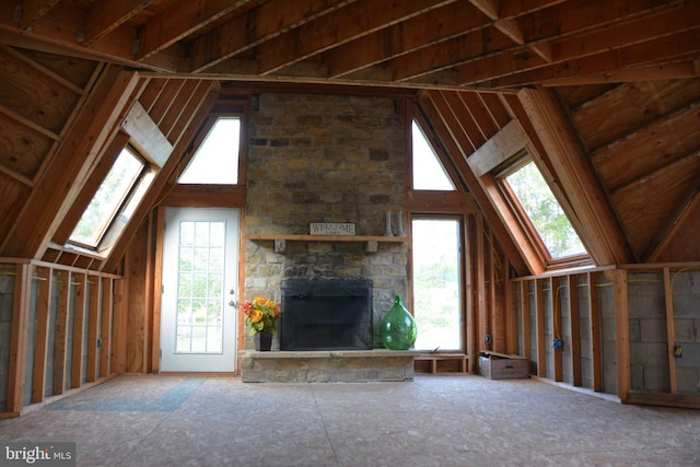 unfurnished living room with a stone fireplace and vaulted ceiling with skylight