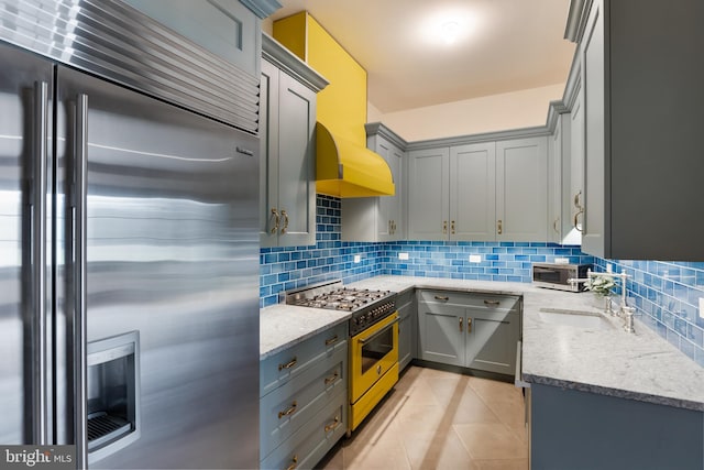 kitchen featuring gray cabinets, sink, backsplash, high end appliances, and light stone counters