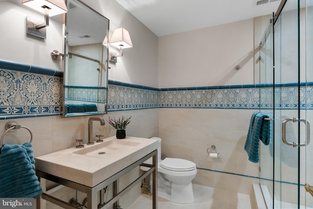 bathroom featuring tile walls, sink, a shower with door, and toilet