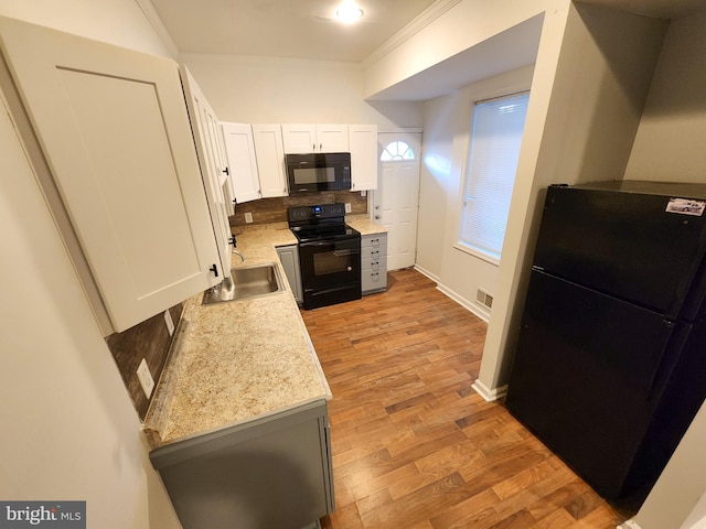 kitchen with white cabinetry, light hardwood / wood-style floors, black appliances, decorative backsplash, and ornamental molding