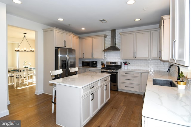 kitchen with appliances with stainless steel finishes, sink, wall chimney exhaust hood, decorative light fixtures, and a center island