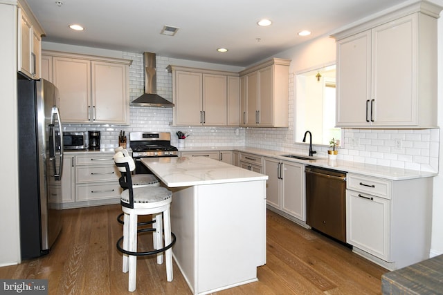 kitchen with wall chimney range hood, appliances with stainless steel finishes, sink, a center island, and hardwood / wood-style flooring