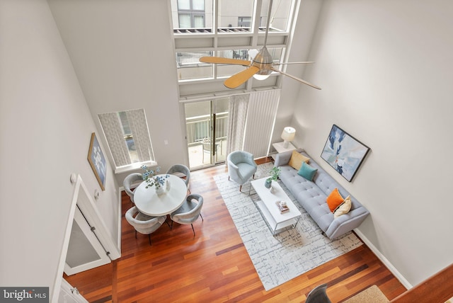 living room with ceiling fan, a towering ceiling, and hardwood / wood-style floors