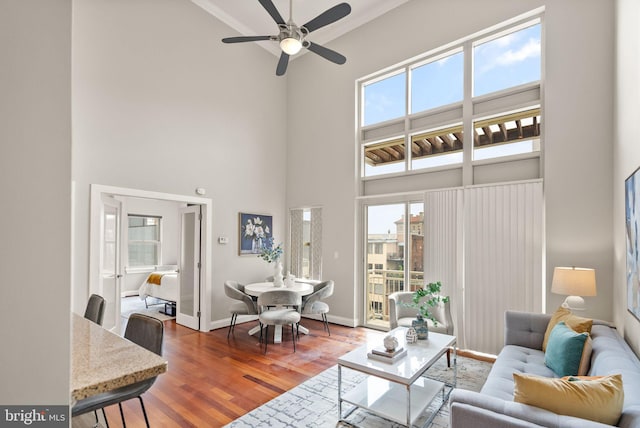 living room with a towering ceiling, hardwood / wood-style flooring, plenty of natural light, and ceiling fan