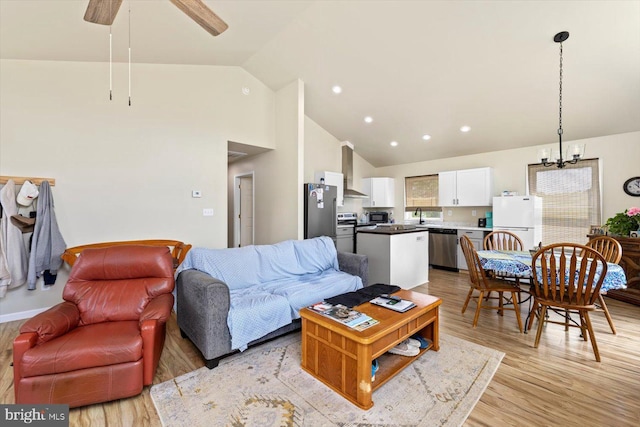 living room with ceiling fan with notable chandelier, sink, vaulted ceiling, and light hardwood / wood-style flooring