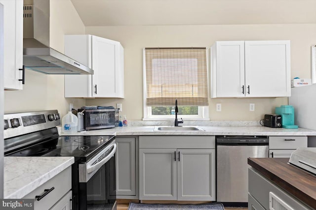 kitchen featuring gray cabinetry, appliances with stainless steel finishes, sink, and wall chimney range hood