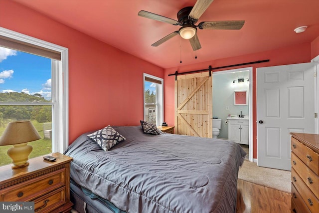 bedroom featuring ensuite bath, light hardwood / wood-style flooring, a barn door, and ceiling fan