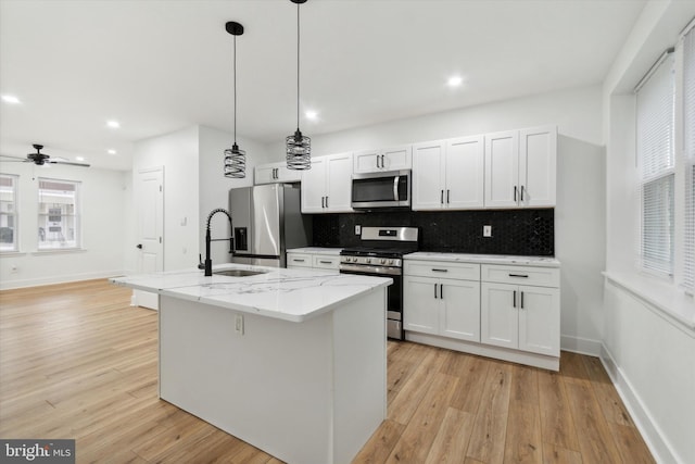 kitchen featuring appliances with stainless steel finishes, white cabinets, a center island with sink, light hardwood / wood-style floors, and light stone countertops