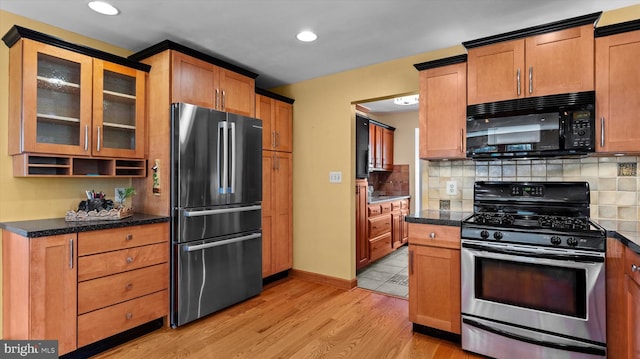 kitchen featuring appliances with stainless steel finishes, dark stone counters, light hardwood / wood-style floors, and decorative backsplash