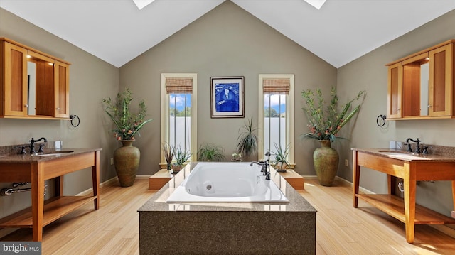 bathroom with a washtub, hardwood / wood-style floors, vanity, and vaulted ceiling with skylight