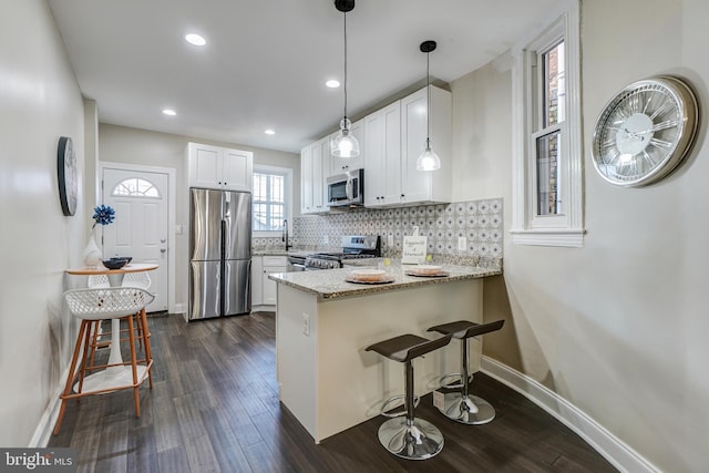 kitchen with appliances with stainless steel finishes, kitchen peninsula, light stone countertops, white cabinetry, and dark hardwood / wood-style flooring