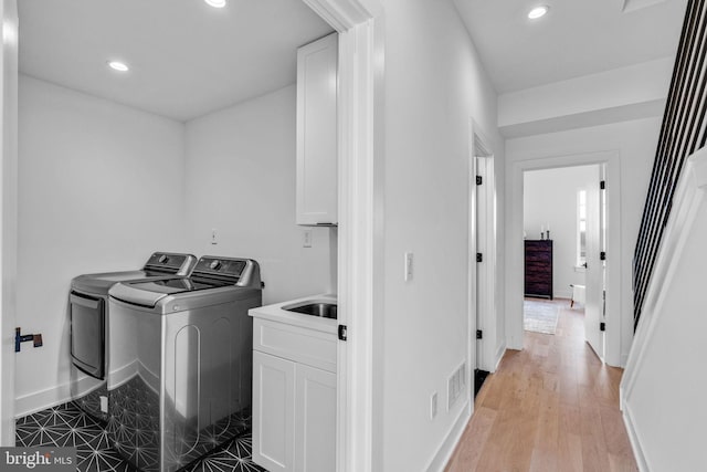 laundry room featuring cabinets, washing machine and dryer, sink, and light hardwood / wood-style flooring